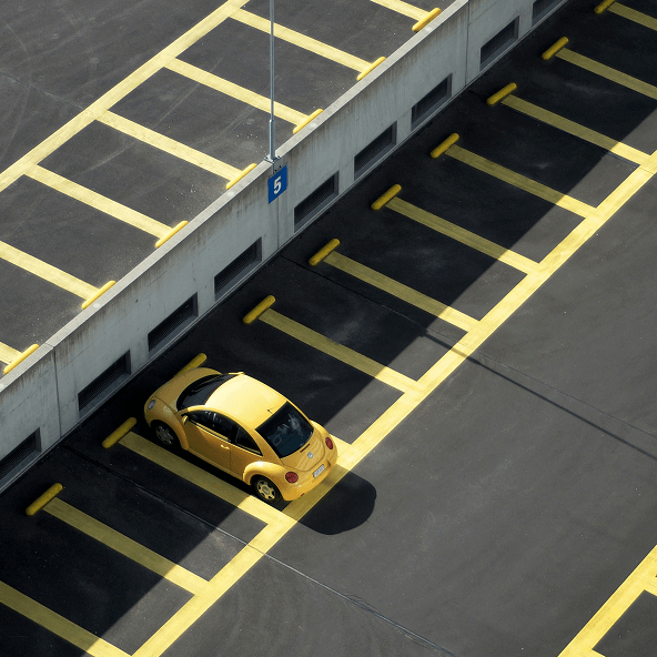 Parking z zaznaczonymi na żółto liniami wyznaczającymi miejsca dla samochodów, na jednym stoi żółte auto.