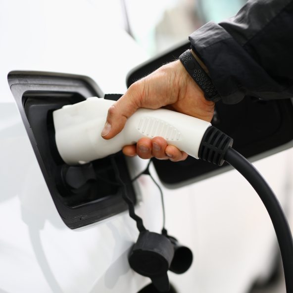 Męska ręka trzyma ładowarkę i ładuje samochód elektryczny
